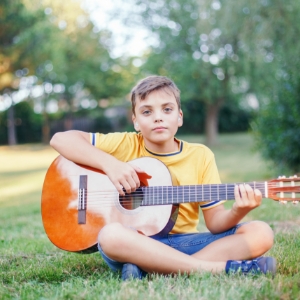 preteen-caucasian-boy-playing-guitar-on-summer-day-92YHXWM.jpg